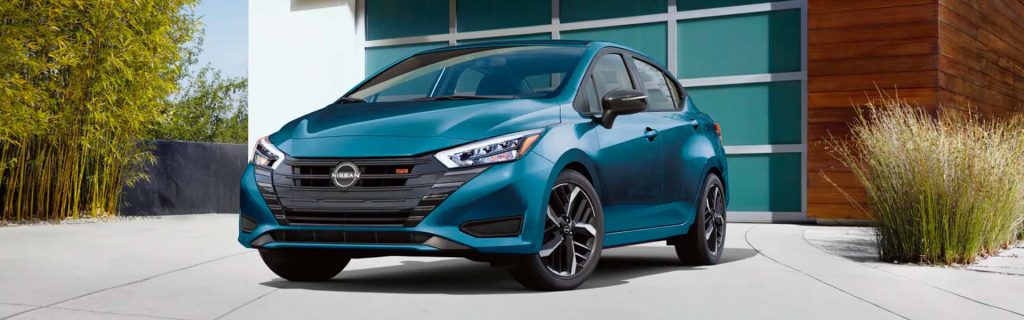 A blue 2025 Nissan Versa parked in front of a modern building with greenery.