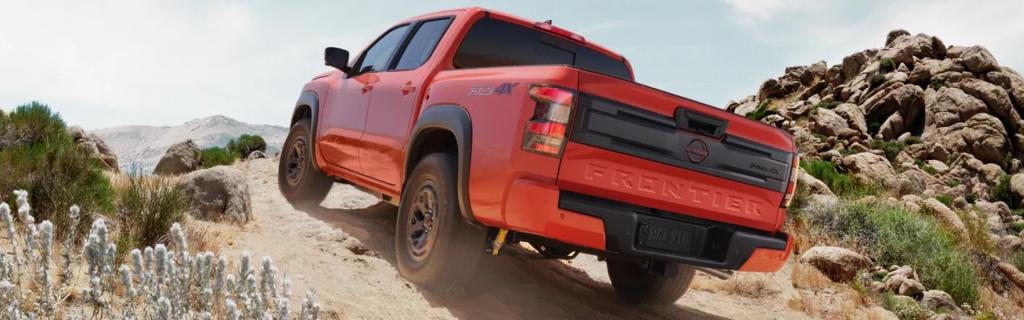 Orange Nissan Frontier PRO-4X pickup truck driving on a rugged desert trail, showcasing its off-road capability and adventurous design.