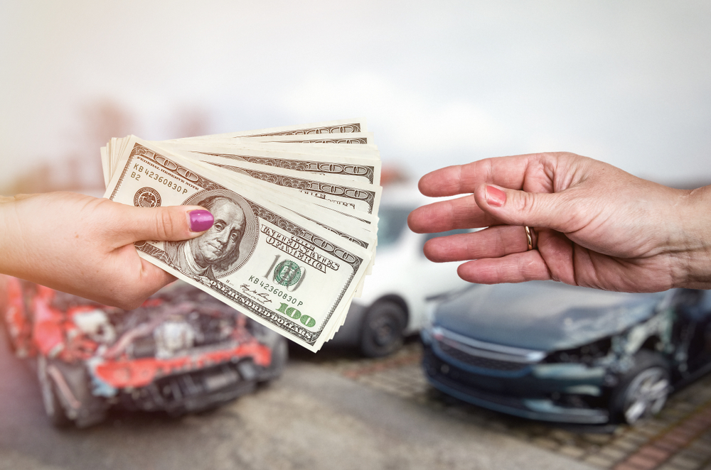 Person handing cash to another person with vehicles in the background.