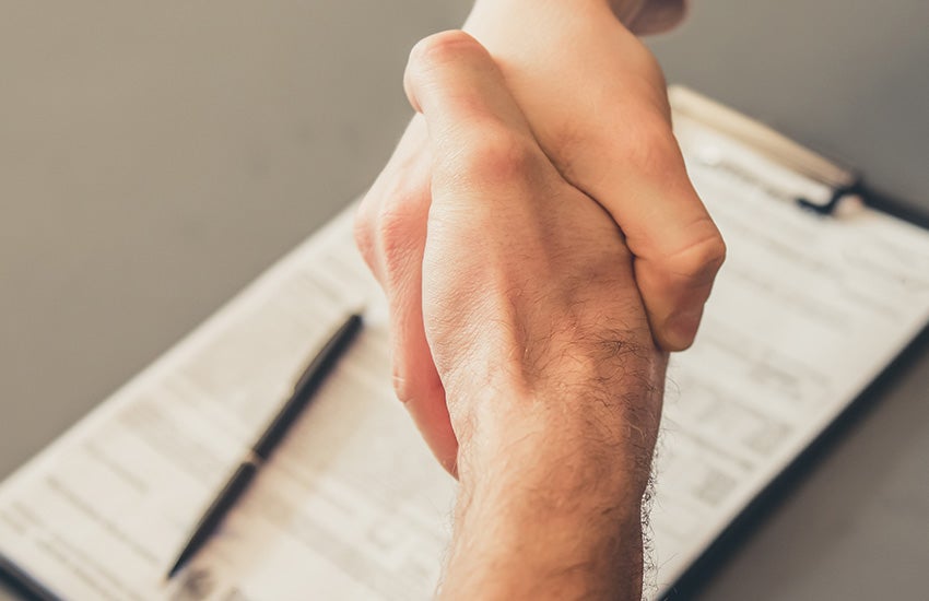 Two people shaking hands over a signed document during a business agreement or vehicle purchase process.
